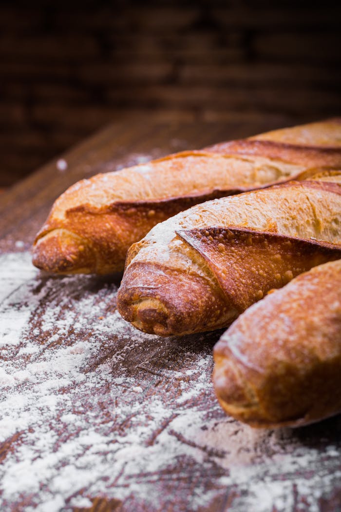 Close-up of fresh, golden-brown baguettes dusted with flour on a wooden table, showing texture and artisan quality.